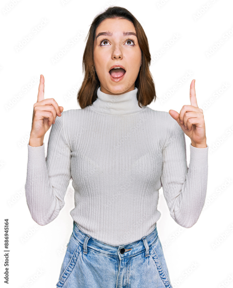 © Krakenimages.com - Young caucasian girl wearing casual clothes amazed and surprised looking up and pointing with fingers and raised arms.