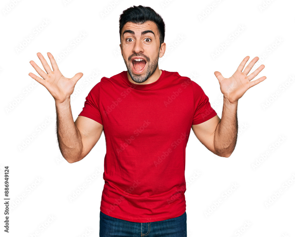 Hispanic man with beard wearing casual red t shirt celebrating crazy and amazed for success with arms raised and open eyes screaming excited. winner concept Hispanic man with beard wearing casual red t shirt celebrating crazy and amazed for success with arms raised and open eyes screaming excited. winner concept