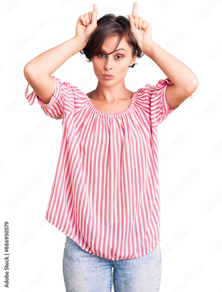 Beautiful young woman with short hair wearing casual summer clothes doing funny gesture with finger over head as bull horns Beautiful young woman with short hair wearing casual summer clothes doing funny gesture with finger over head as bull horns
