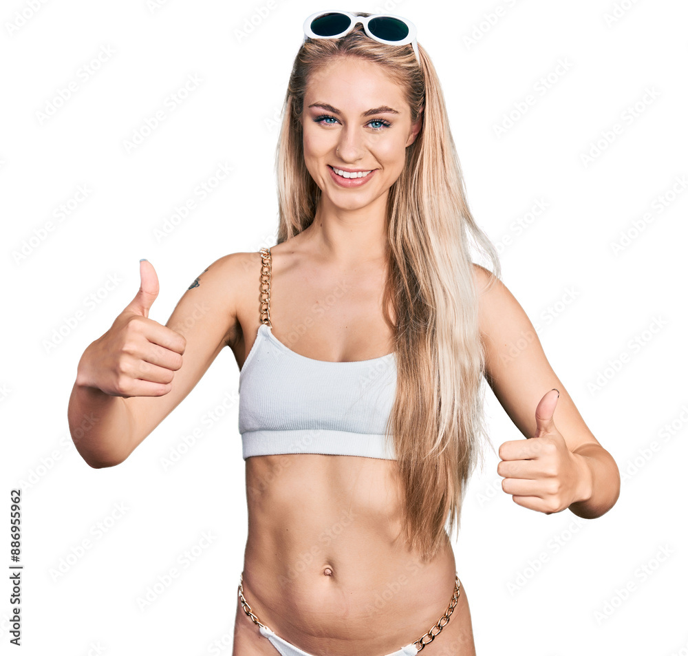 Beautiful young blonde woman wearing bikini success sign doing positive gesture with hand, thumbs up smiling and happy. cheerful expression and winner gesture. Beautiful young blonde woman wearing bikini success sign doing positive gesture with hand, thumbs up smiling and happy. cheerful expression and winner gesture.