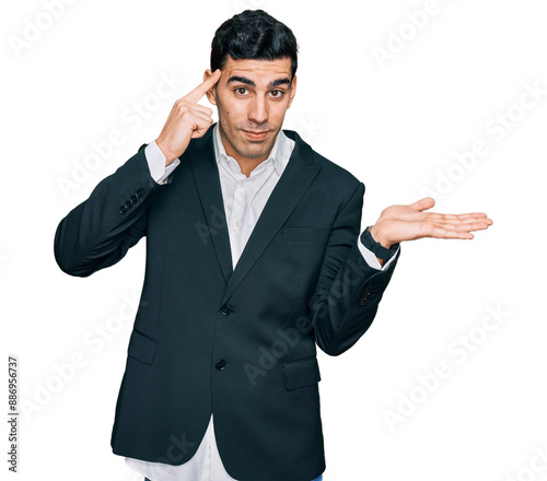 Handsome hispanic man wearing business clothes confused and annoyed with open palm showing copy space and pointing finger to forehead. think about it.