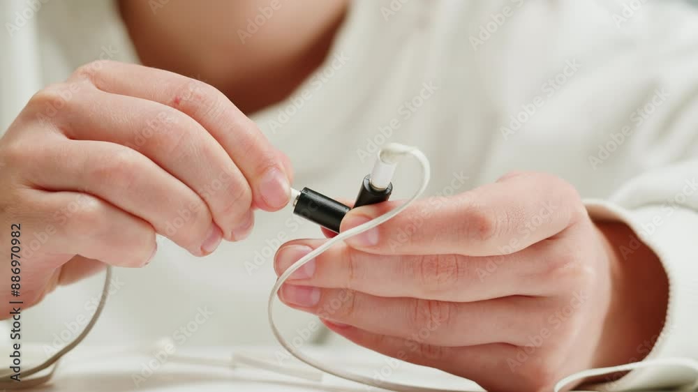 Young woman trying to untangle the headphones close-up. Special adapter for headphone. Tangled wires on table. Trying to untangle many messy cables Young woman trying to untangle the headphones close-up. Special adapter for headphone. Tangled wires on table. Trying to untangle many messy cables
