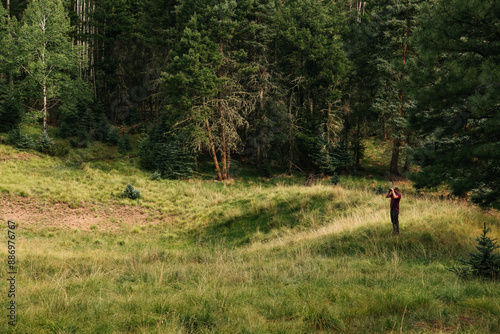 A man in a camouflage jacket stands looking through binoculars in a clearing while hunting for Elk in the Valles Caldera National Preserve, New Mexico photo