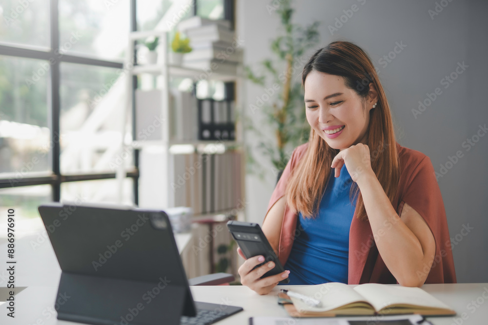Happy asian businesswoman reads a text on her smartphone in a modern office, showing the positive impact of technology on work life