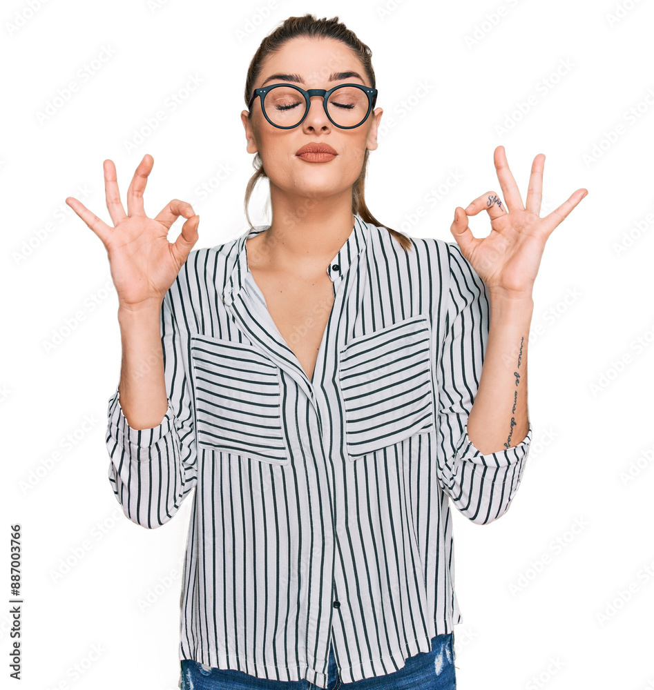 Young caucasian woman wearing business shirt and glasses relax and smiling with eyes closed doing meditation gesture with fingers. yoga concept. Young caucasian woman wearing business shirt and glasses relax and smiling with eyes closed doing meditation gesture with fingers. yoga concept.