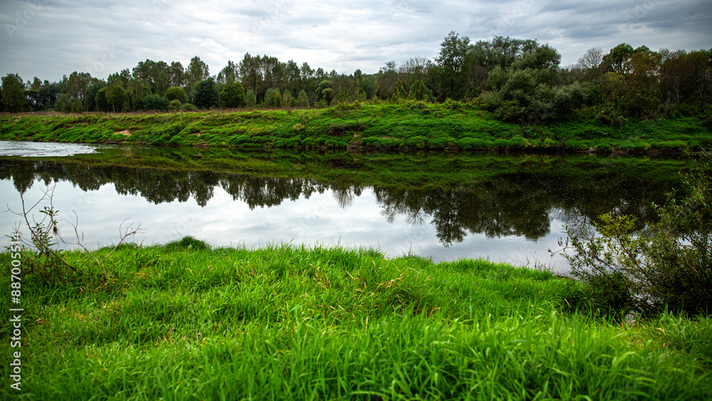 Fototapeta premium Enjoy a tranquil river landscape surrounded by lush greenery, reflected in calm waters
