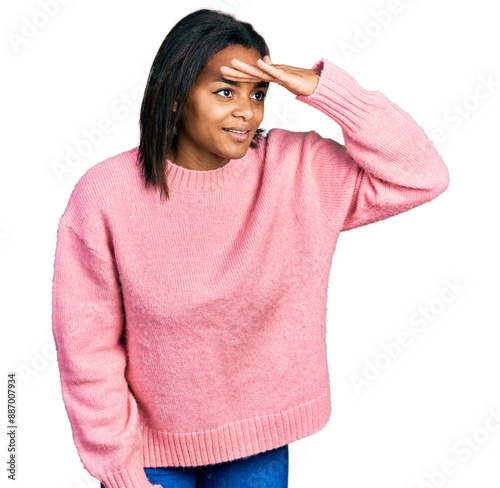 Beautiful hispanic woman wearing casual winter sweater very happy and smiling looking far away with hand over head. searching concept.