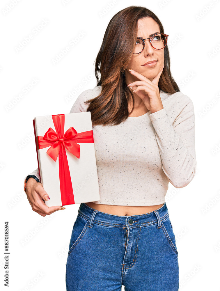 Young brunette woman holding gift serious face thinking about question with hand on chin, thoughtful about confusing idea Young brunette woman holding gift serious face thinking about question with hand on chin, thoughtful about confusing idea