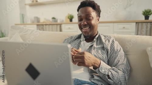 Young African American man chatting by video call by laptop at home, portrait. Joyful person smiling broadly and talking cheerfully with friends, online communication by internet, positive emotions