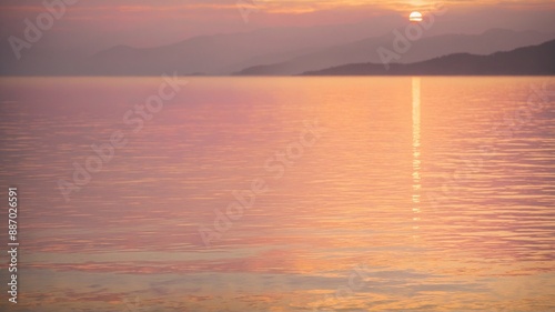 A breathtaking sunset scene over a calm sea, with the warm hues of orange, pink, and purple painting the sky and reflecting on the water. The silhouettes of distant mountains.