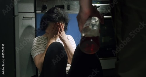 Frightened woman abused victim by man alcoholic, scared wife sitting on the floor in kitchen, crying. Family problems, alcohol addicted, aggressive husband, boyfriend. Domestic violence concept
