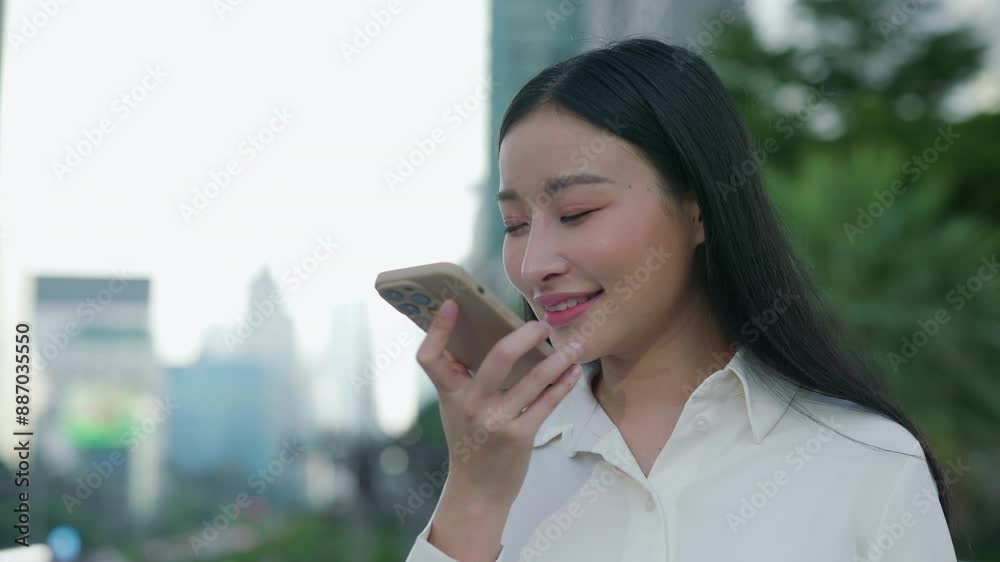 Asian Woman Standing and Recording a Voice SMS, Smiling at the Phone. Asian Woman Standing and Recording a Voice SMS, Smiling at the Phone.