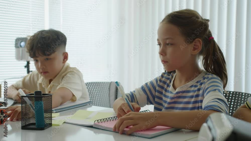 Handheld shot of two bi-ethnic elementary school pupils studying at desk when doing test Handheld shot of two bi-ethnic elementary school pupils studying at desk when doing test