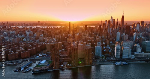 Flight over the East River at sunset time. Revealing view on splendid New York in the orange light of setting sun.