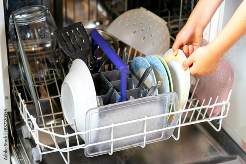 Children's hands load dirty dishes into the dishwasher photo