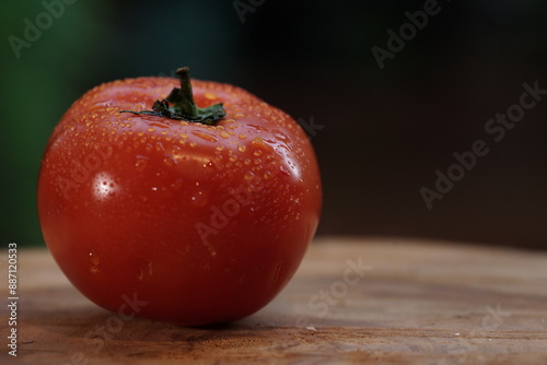 A vibrant red tomato with water drops on a dark background, highlighting its freshness and juiciness. Ideal for culinary, health and organic themed projects.