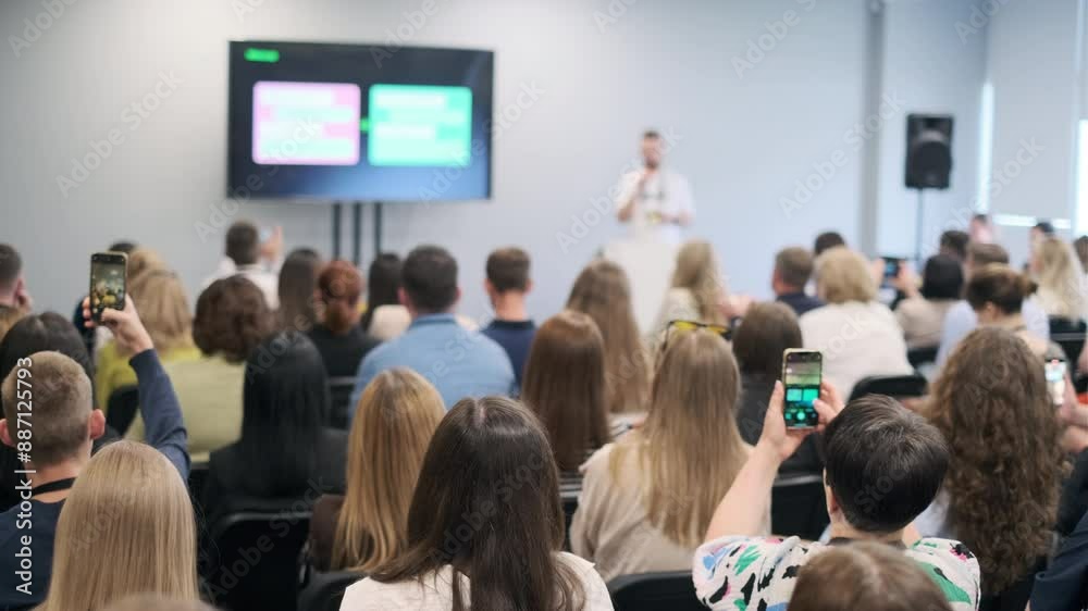 Diverse audience attentively listening to a speaker presenting at a business seminar in a conference room. Shows engagement, focus, and professional environment.