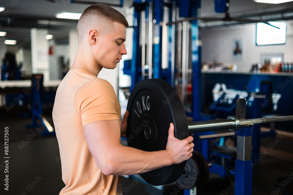 Bodybuilder lifts a weight plate during his workout at the gym Bodybuilder lifts a weight plate during his workout at the gym
