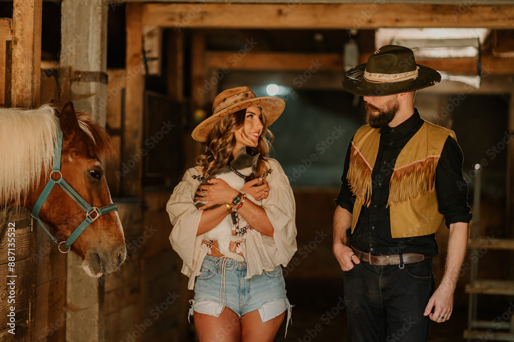 Rancher couple with cat is smiling at each other at ranch in horse stall Rancher couple with cat is smiling at each other at ranch in horse stall