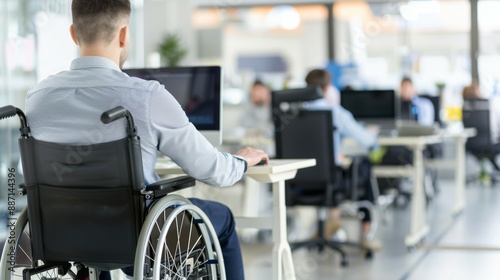 A man in a wheelchair is sitting at a desk in front of a computer, people with disabilities at work