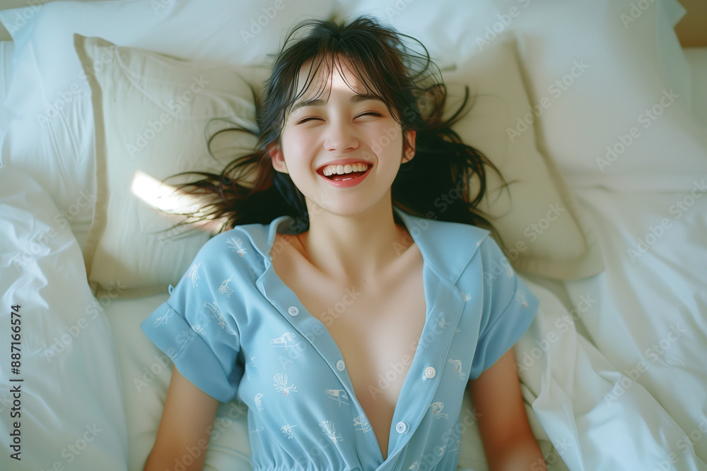 水色のパジャマを着て、ベッドの上で笑っている女性 水色のパジャマを着て、ベッドの上で笑っている女性