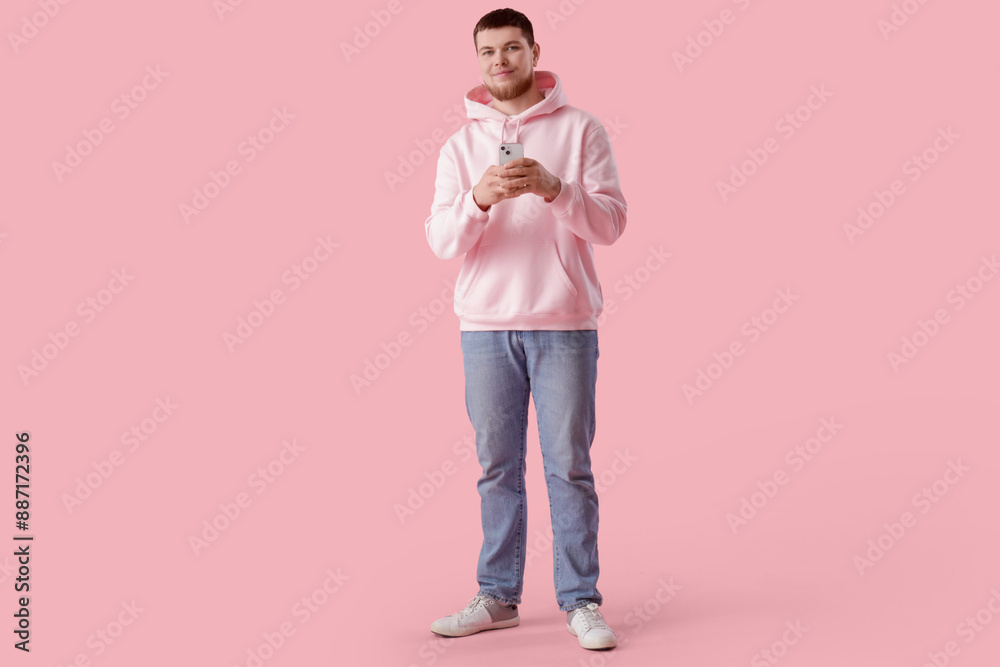 Young bearded man using mobile phone on pink background