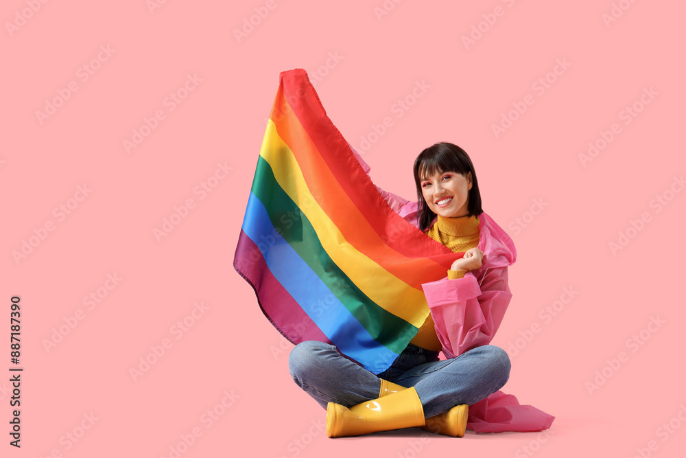 Beautiful young woman with LGBT flag sitting on pink background Beautiful young woman with LGBT flag sitting on pink background