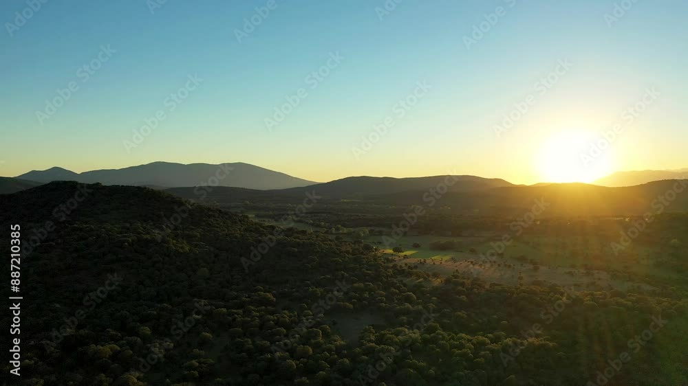 Backlit drone filming in the spectacular Tiétar Valley where we see hills full of green trees, meadows, a mountain system in the background with a blue sky and striking flashes produced by the sun. Backlit drone filming in the spectacular Tiétar Valley where we see hills full of green trees, meadows, a mountain system in the background with a blue sky and striking flashes produced by the sun.