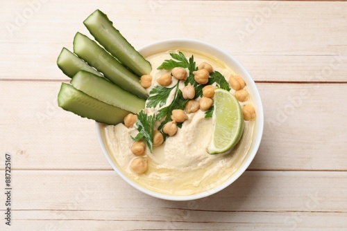 Tasty hummus with chickpeas, cucumber and lime in bowl on wooden table, top view photo