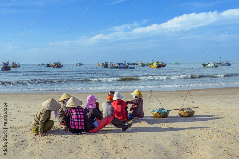 Scene of women sitting on the beach in the early morning and waiting for the fishing boat to return from the sea in Ke Ga, Binh Thuan province, Vietnam