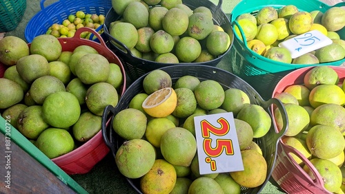 collection of baskets, filled with green grapefruits, sit on a table, for sale at a market in Thailand.
