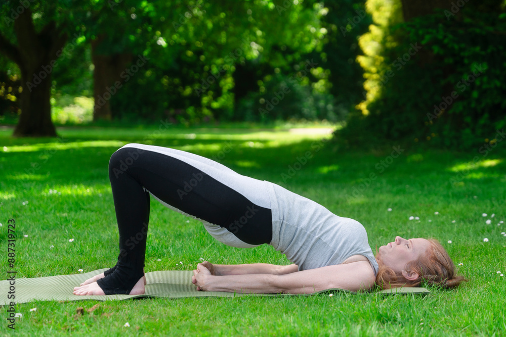 Fototapeta premium Woman Performing Bridge Pose on Green Grass in a Park