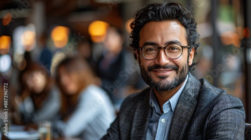 A man with a beard and glasses smiles warmly while sitting at a table in a cafe