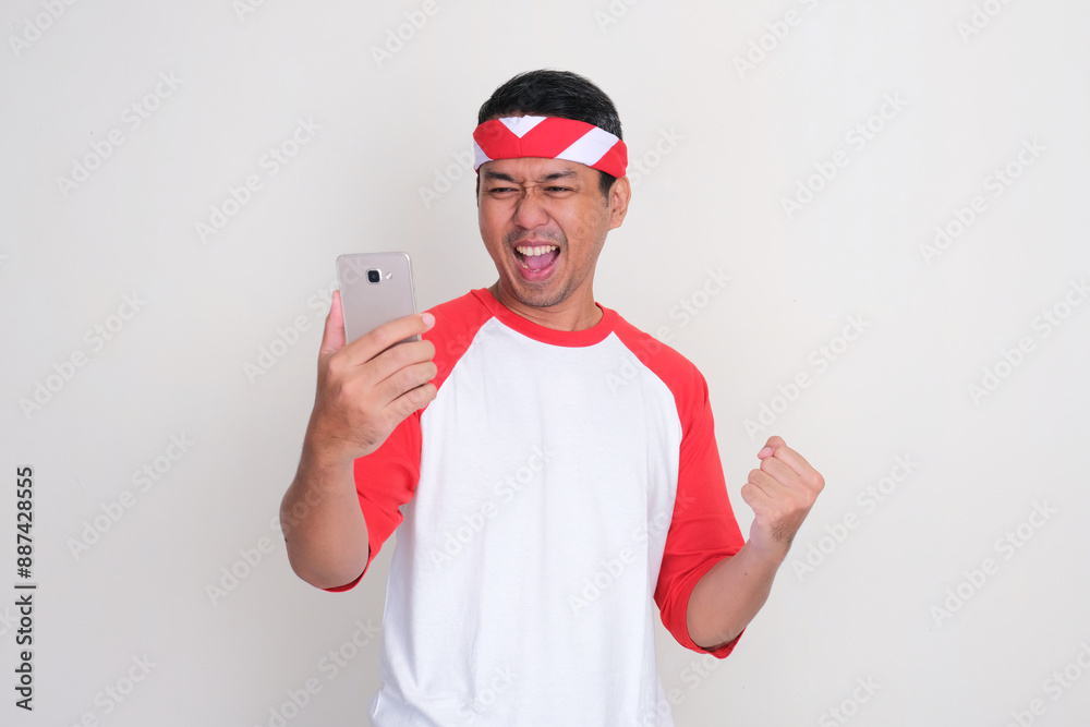 Indonesian man clenched fist showing excitement when looking to his mobile phone
