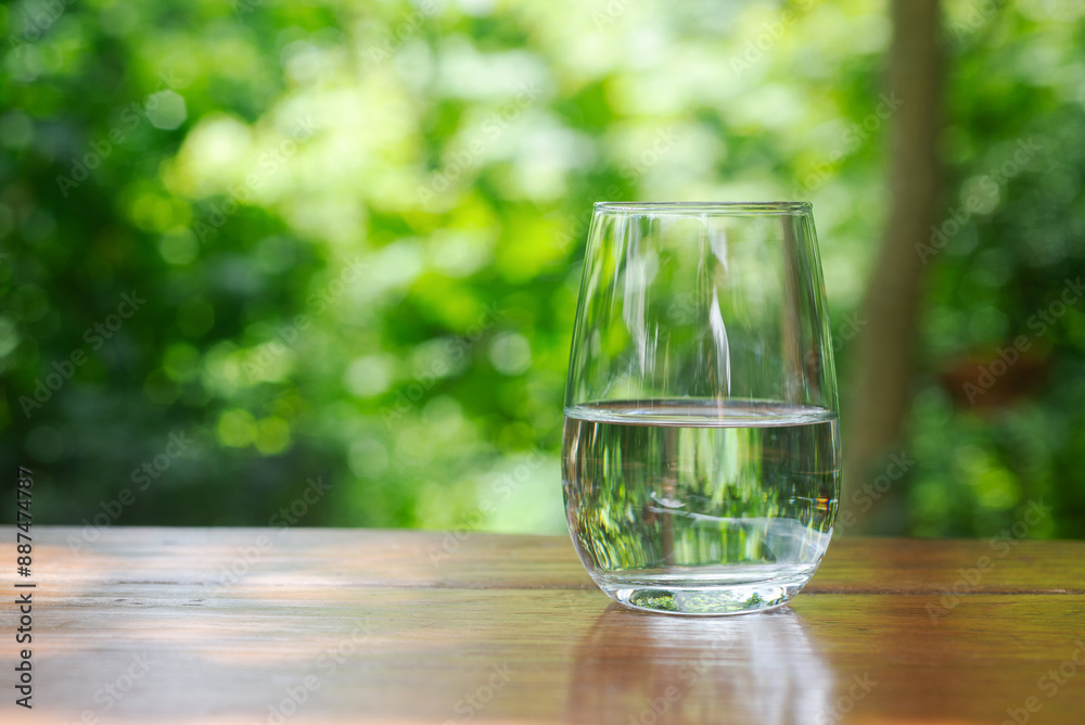 half glass of drinking water on wooden table in garden with green bokeh background. half glass of drinking water on wooden table in garden with green bokeh background.