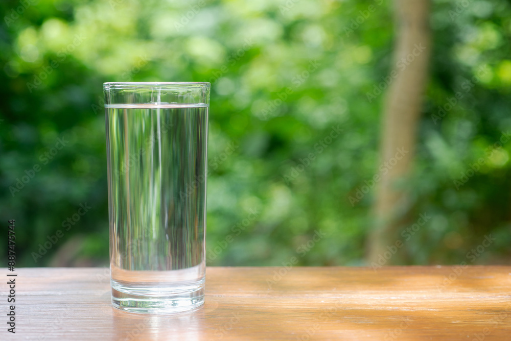 Drinking  water in tall glass on wooden table in garden background.