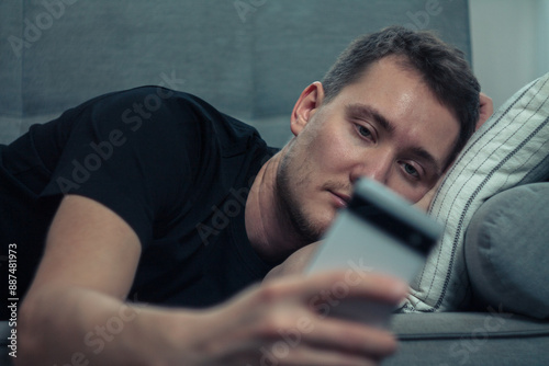 Fotografie A man is procrastinating: sitting with a phone in his hands, relaxed position, c