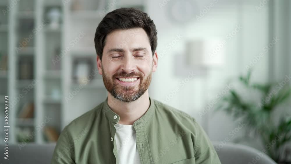 Portrait of happy handsome man sitting on sofa in living room at home. Head shot of confident smiling bearded businessman in shirt. Positive mature male poses looking at camera indoors. Close up Portrait of happy handsome man sitting on sofa in living room at home. Head shot of confident smiling bearded businessman in shirt. Positive mature male poses looking at camera indoors. Close up