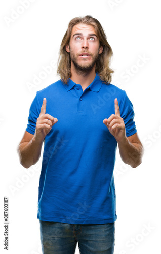 Young handsome man with long hair over isolated background amazed and surprised looking up and pointing with fingers and raised arms.