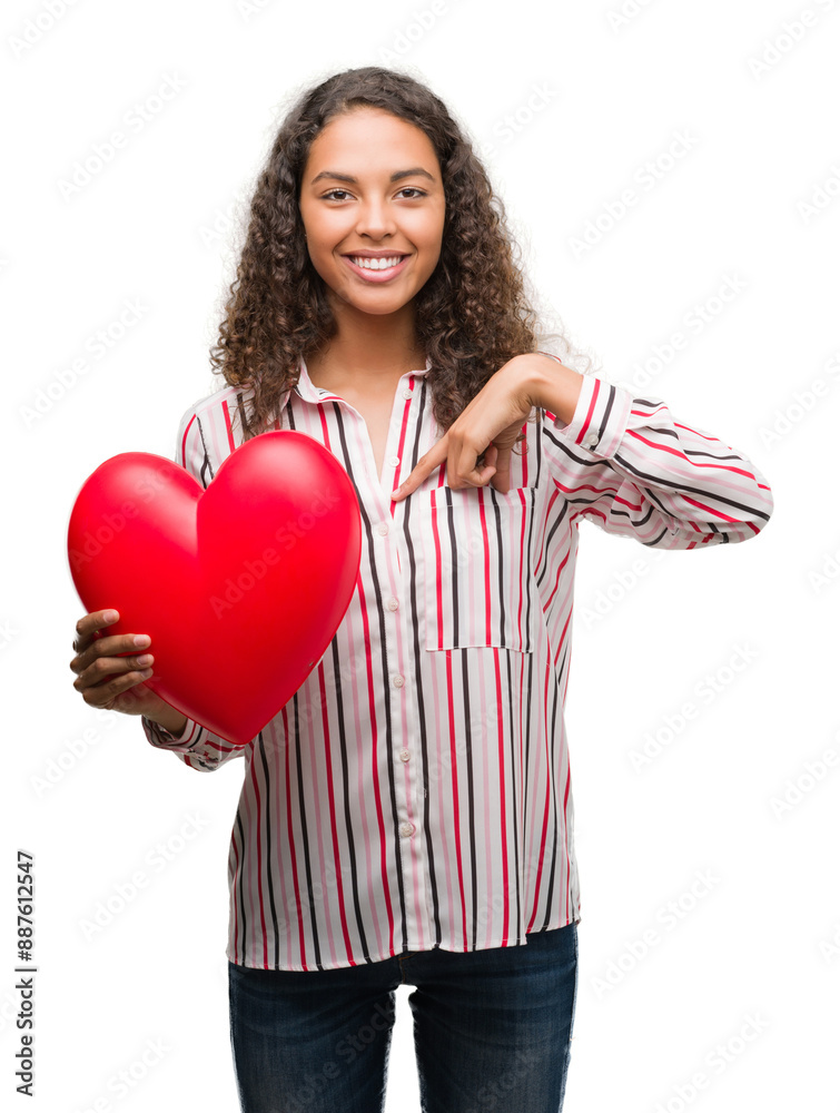 Young hispanic woman in love holding red heart with surprise face pointing finger to himself Young hispanic woman in love holding red heart with surprise face pointing finger to himself