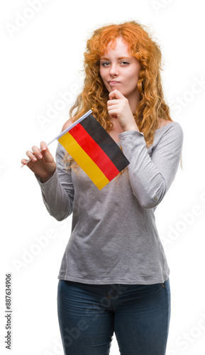 Young redhead woman holding flag of Germany serious face thinking about question, very confused idea