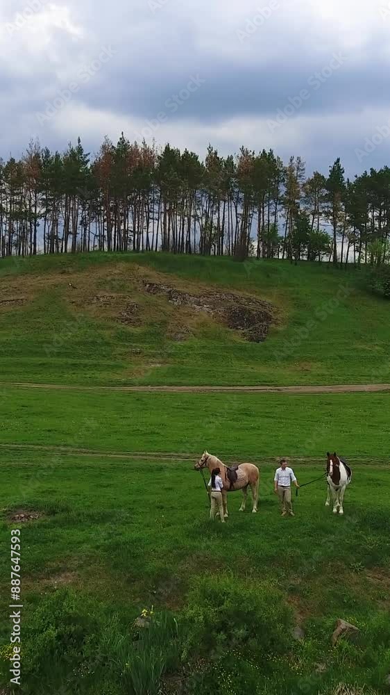 Couple standing at the river bank holding horses. Lovely date in the nature on summer day. Beautiful meadow and woods at backdrop. Vertical video Couple standing at the river bank holding horses. Lovely date in the nature on summer day. Beautiful meadow and woods at backdrop. Vertical video