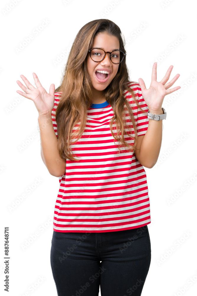 Young beautiful brunette woman wearing glasses and stripes t-shirt over isolated background celebrating crazy and amazed for success with arms raised and open eyes screaming excited. Winner concept Young beautiful brunette woman wearing glasses and stripes t-shirt over isolated background celebrating crazy and amazed for success with arms raised and open eyes screaming excited. Winner concept