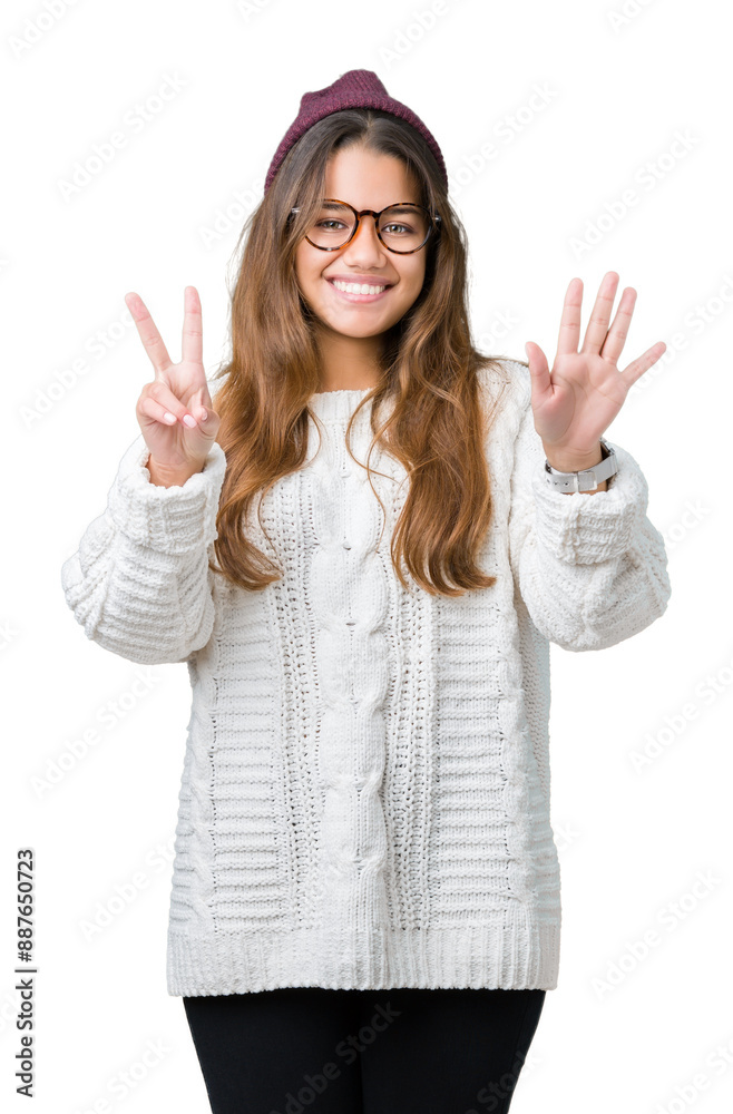 Young beautiful brunette hipster woman wearing glasses and winter hat over isolated background showing and pointing up with fingers number seven while smiling confident and happy.