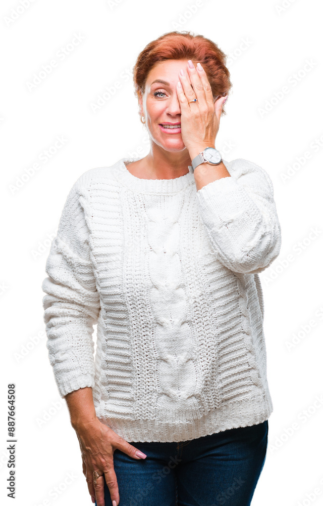Atrractive senior caucasian redhead woman wearing winter sweater over isolated background covering one eye with hand with confident smile on face and surprise emotion.