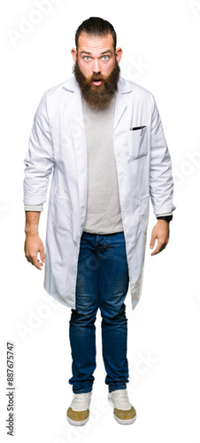 Young blond scientist man wearing white coat afraid and shocked with surprise expression, fear and excited face.