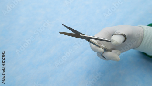 Hand in white glove holds stainless medical scissor. This stainless steel stainless medical scissor used in surgery. Surgical instruments. Equipment use in surgery. Medical equipment.