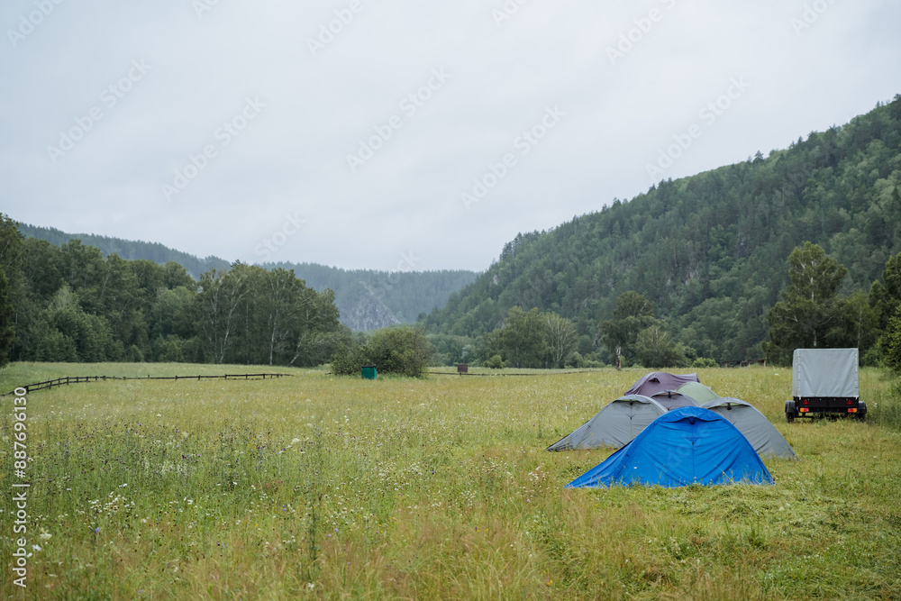 In the tranquil setting of a grassy field, a striking blue tent is positioned amidst lush trees and greenery under a clear sky. The scene evokes a sense of serenity and peace In the tranquil setting of a grassy field, a striking blue tent is positioned amidst lush trees and greenery under a clear sky. The scene evokes a sense of serenity and peace