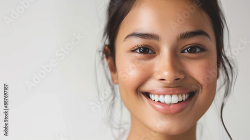 Against a white background is a close-up portrait photo of a beautiful young woman of Asian descent smiling with flawless teeth. 