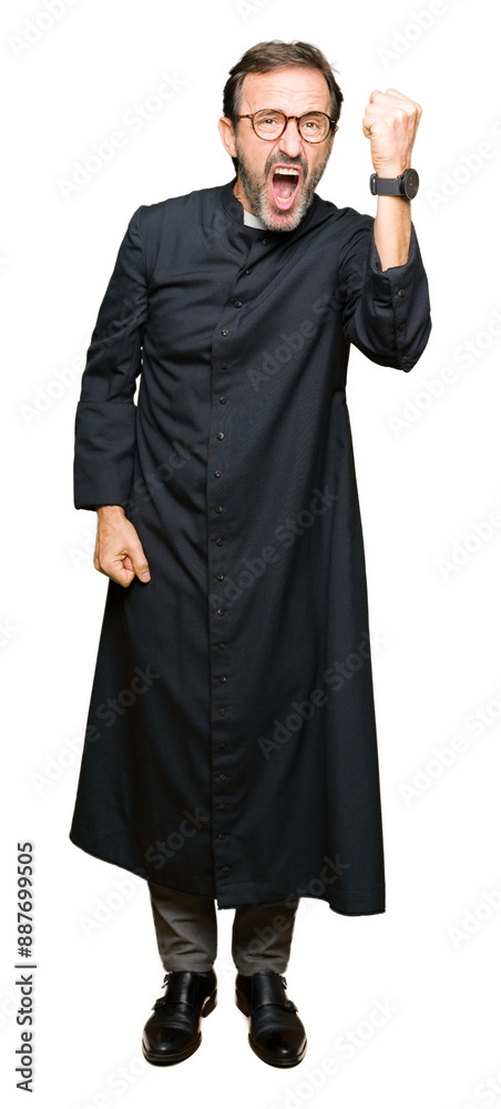 Middle age priest man wearing catholic robe angry and mad raising fist frustrated and furious while shouting with anger. Rage and aggressive concept. Middle age priest man wearing catholic robe angry and mad raising fist frustrated and furious while shouting with anger. Rage and aggressive concept.